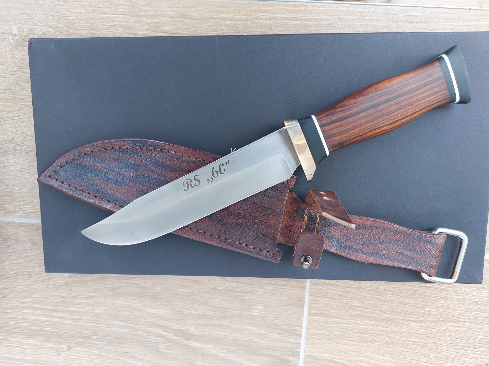 Nůž z Elmaxu, rukojeť kombinace bronzu, G10, Corianu a železného dřeva Desert Ironwood. Upevněno na trn se skrytou maticí.